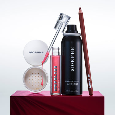 Morphe makeup products including a setting mist, brush, and other items on a red platform with a white background.